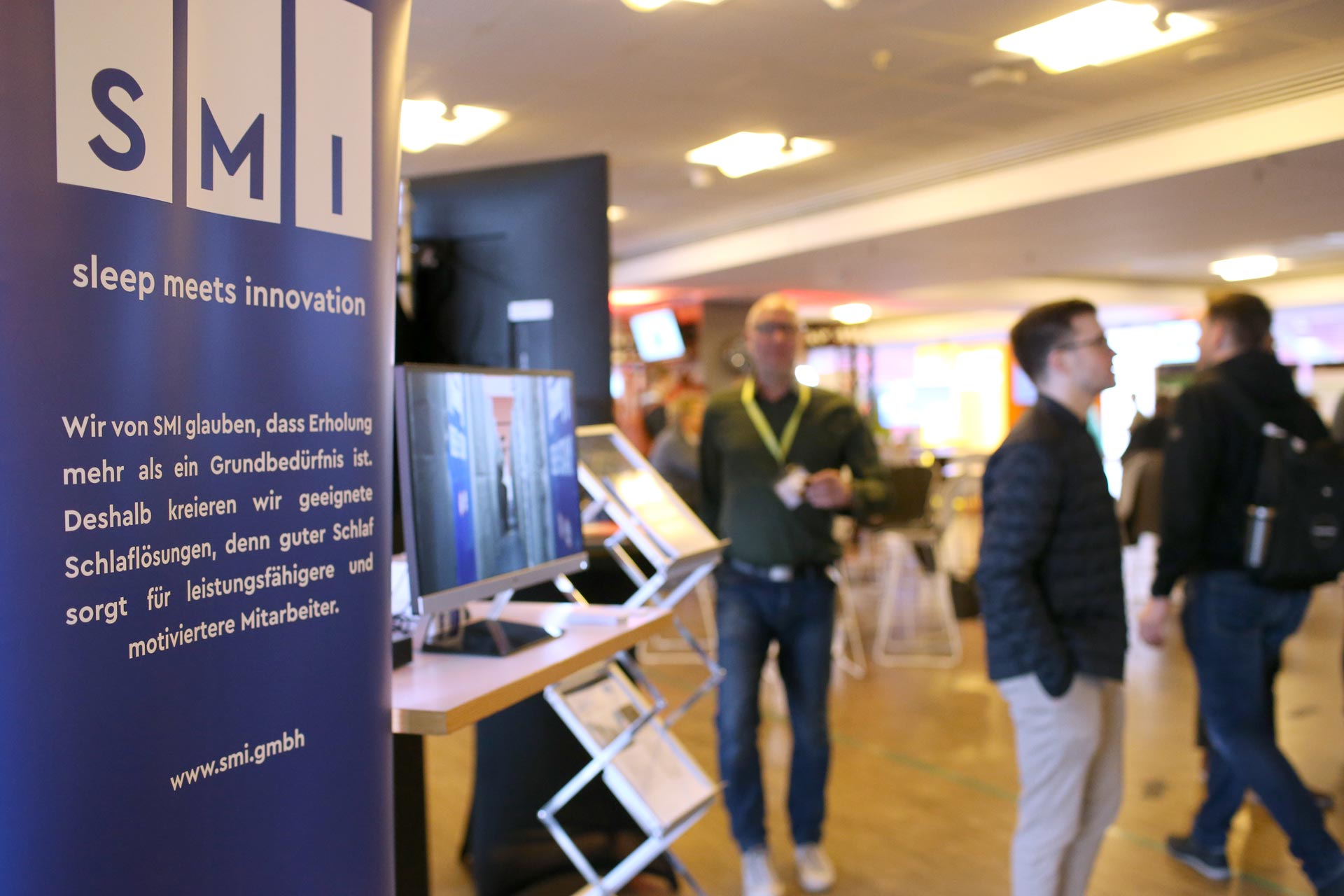 Menschen stehen an einem Informationsstand, während eine Veranstaltung zum Thema Sicherheit im Eventbereich stattfindet. IBIT.