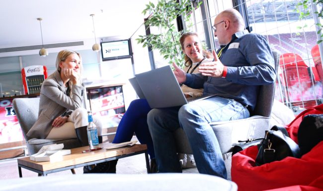 Drei Personen diskutieren in einer modernen Umgebung, umgeben von Pflanzen und Laptops. IBIT-Weiterbildung Veranstaltungssicherheit.