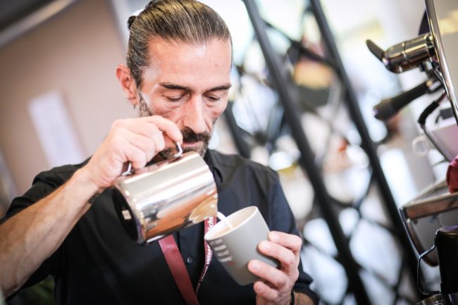 Ein Barista bereitet mit Präzision einen Kaffee in einem modernen Veranstaltungsraum, ideal für IBIT-Events.