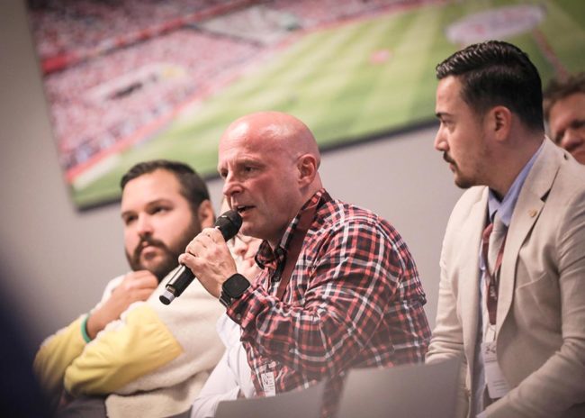 Podiumsddiskussion während einer IBIT-Fachtagung Veranstaltungssicherheit mit drei Sprechern und sportlicher Kulisse.