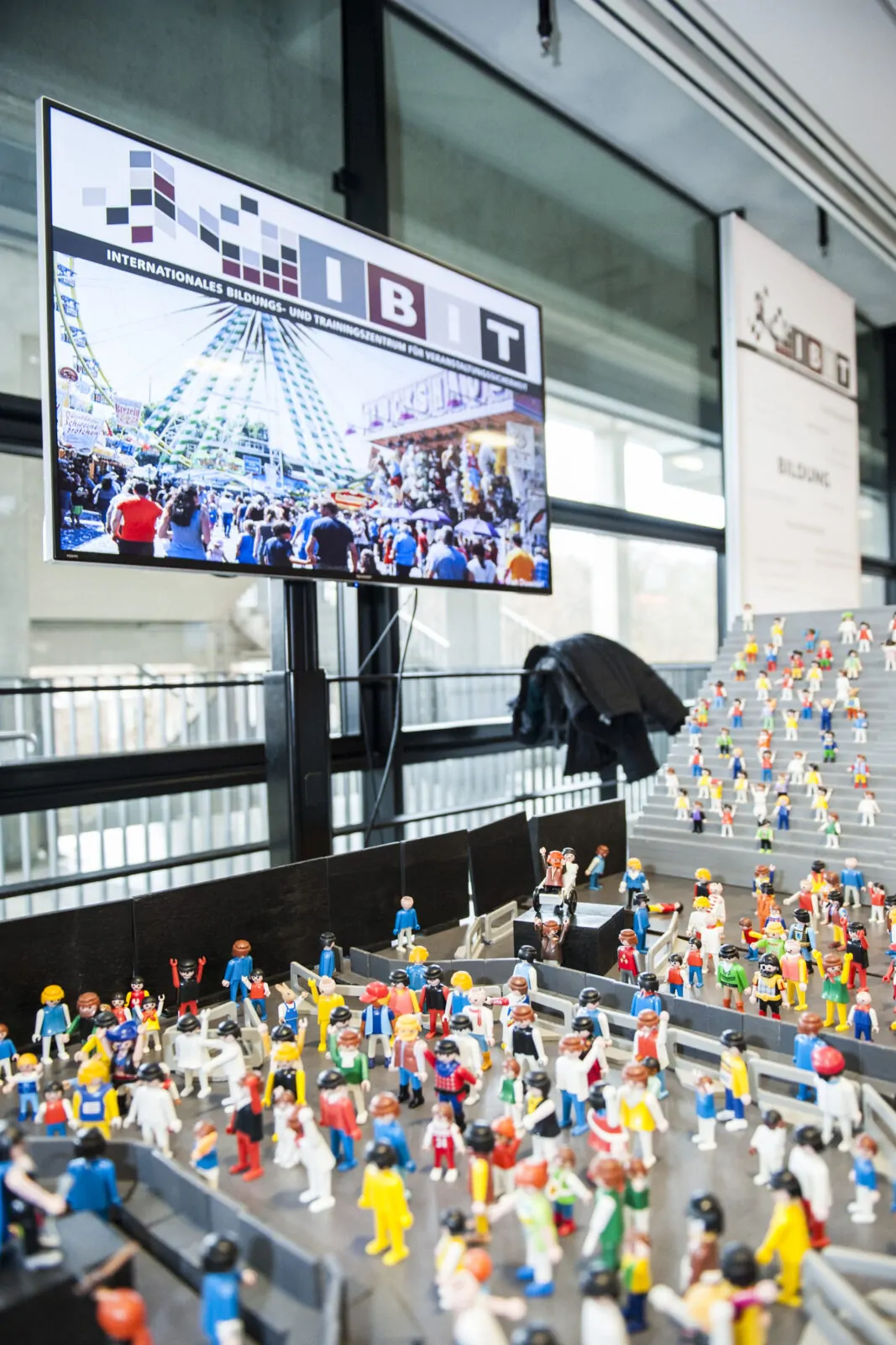 Modellierte Figuren und ein Bildschirm mit Veranstaltungsszenen im IBIT, die Sicherheit bei Events thematisieren.