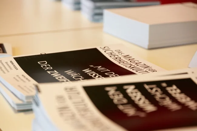 Zwei Broschüren zu Veranstaltungssicherheit liegen auf einem Tisch, umgeben von weiteren Materialien im IBIT-Kontext.