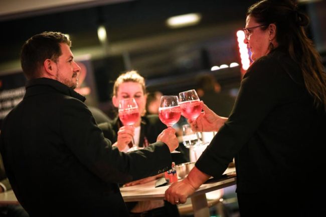 Personen in eleganter Kleidung stoßen mit Getränken an. Die Atmosphäre ist festlich, passend zur IBIT-Veranstaltung.