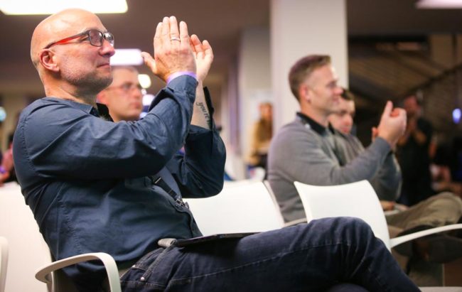 Teilnehmer bei der IBIT-Fachtagung Veranstaltungssicherheit applaudieren begeistert in einem modernen Konferenzraum.