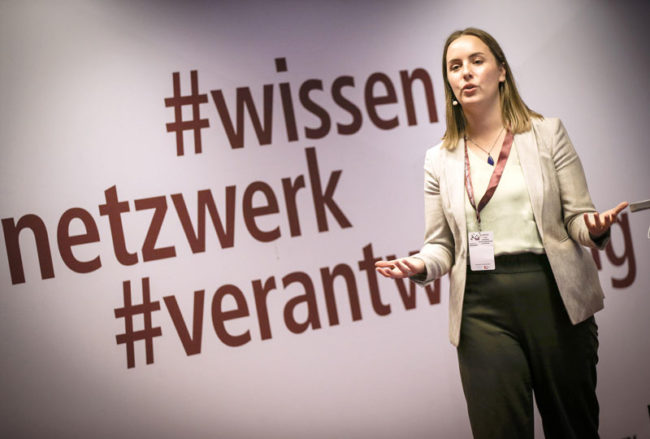 Eine Referentin präsentiert auf der IBIT-Fachtagung Veranstaltungssicherheit vor einem großen Schriftzug mit Hashtags.