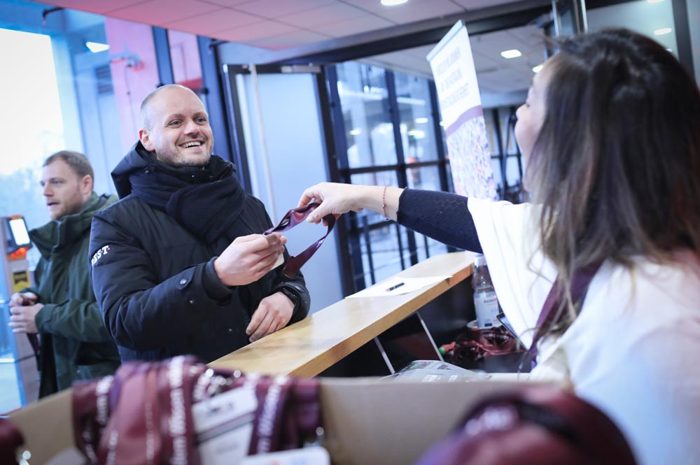 Person an Empfangstheke erhält ein Namensschild von einer Mitarbeiterin. Freundliche Atmosphäre, IBIT-Event.