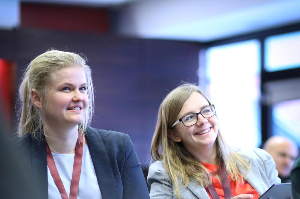 Zwei Frauen in formeller Kleidung lächeln während einer Veranstaltung im IBIT, umgeben von einer professionellen Atmosphäre.