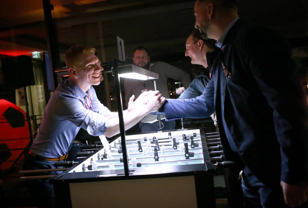 Freundliche Interaktion zwischen Teilnehmern an einem Kicker-Tisch während einer IBIT-Veranstaltung.