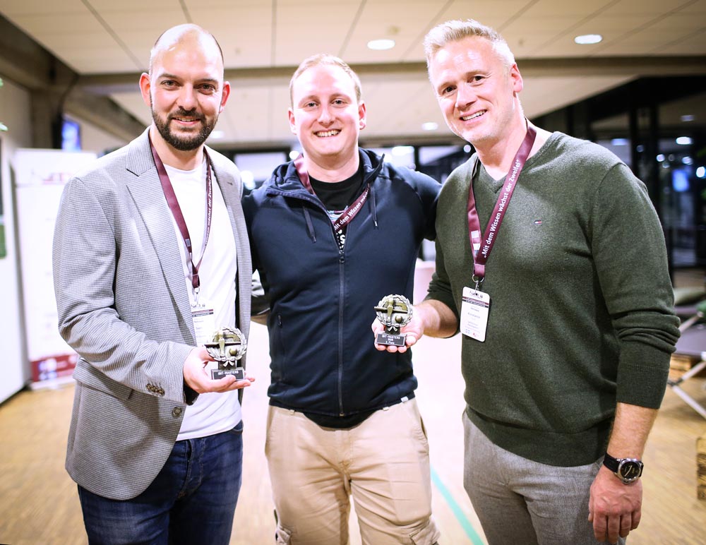 Drei Männer lächeln in einer modernen Umgebung, halten Auszeichnungen in den Händen. Stimmung: feierlich. IBIT.