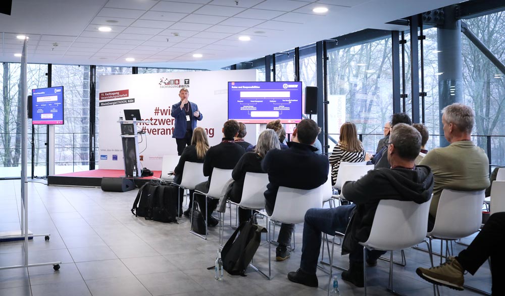 Teilnehmer einer IBIT-Fachtagung Veranstaltungssicherheit hören einem Vortrag in moderner Umgebung mit großen Fenstern zu.